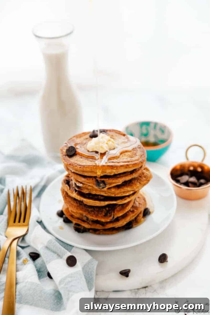 These pumpkin chocolate chip pancakes are prepped in 10 minutes! Made with pumpkin pie spice and pumpkin puree, they're perfect for fall. A plate of pumpkin chocolate chip pancakes, generously drizzled with maple syrup and sprinkled with chocolate chips.