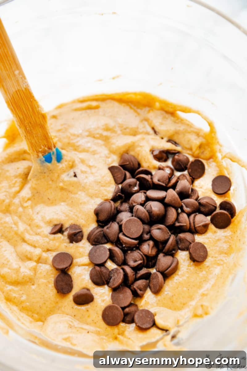 These pumpkin chocolate chip pancakes are prepped in 10 minutes! Made with pumpkin pie spice and pumpkin puree, they're perfect for fall. Stirring pancake batter with chocolate chips in a glass bowl.