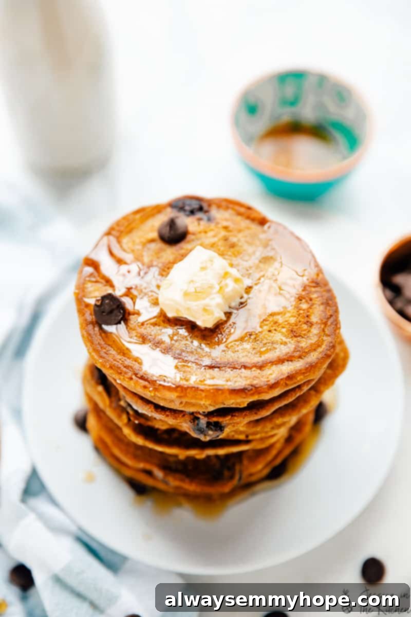 Top down view of a stack of vegan pumpkin chocolate chip pancakes with chocolate chips and maple syrup.