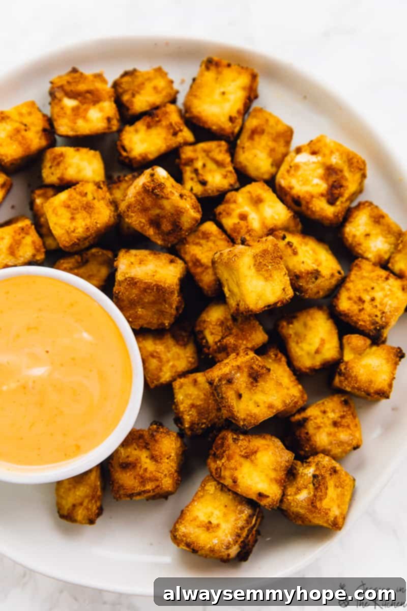 Overhead shot of perfectly baked tofu with a side of dipping sauce.