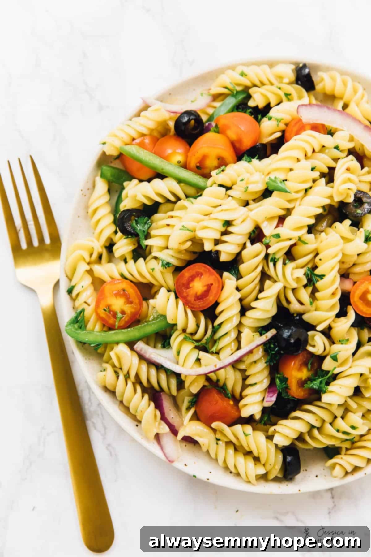 Top down view of vegan pasta salad on a plate next to a gold fork, ready to be enjoyed.
