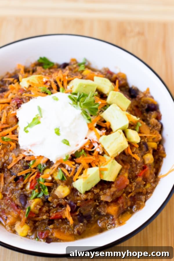 A bowl of quinoa chili topped with diced avocado, vegan cheese, and sour cream.