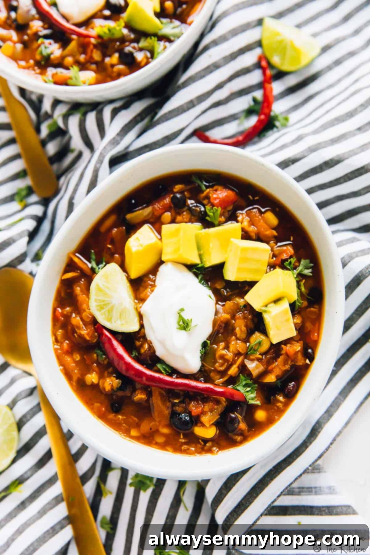 Overhead view of red lentil chili in a bowl, garnished with avocado and a dollop of cream.
