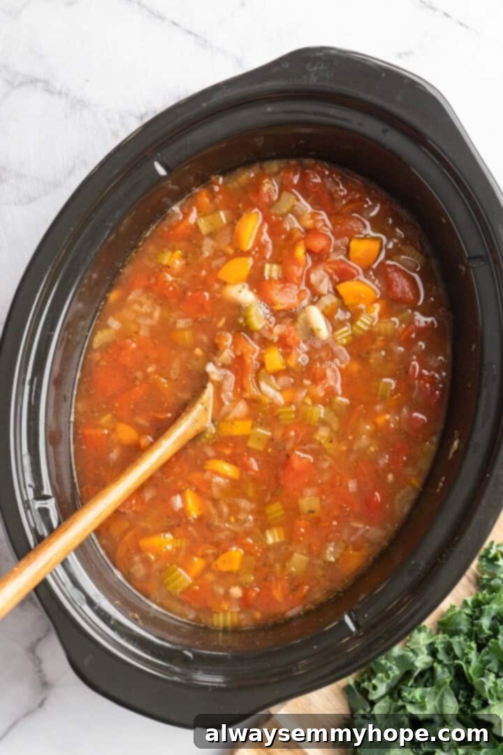 Overhead view of white bean and kale soup simmering in slow cooker before kale is added
