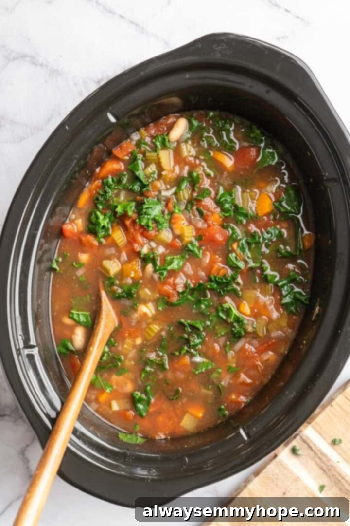 Overhead view of finished white bean and kale soup in slow cooker, with kale wilted