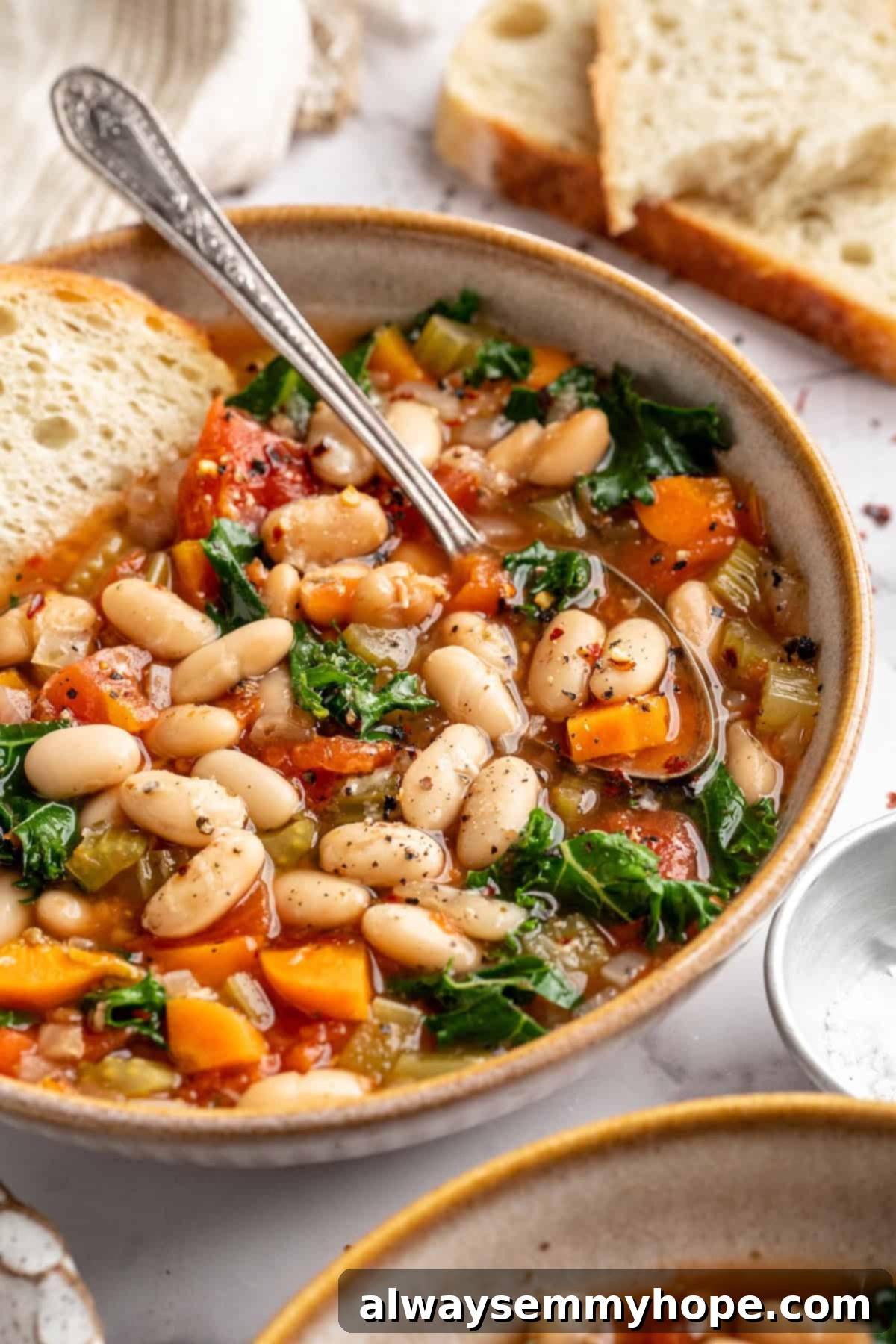 White bean and kale soup in bowl with spoon and a side of crusty bread