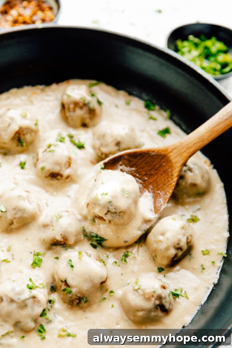 Vegan Swedish meatballs simmering in a skillet with a wooden spoon
