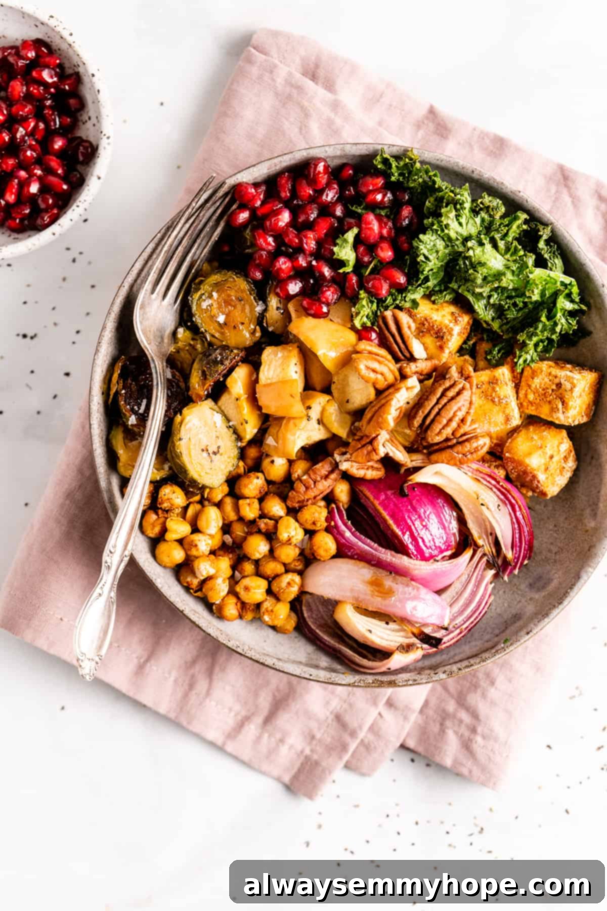 This vegan Buddha bowl is a flavor-packed meal brimming with caramelised roasted veggies, crispy chickpeas, tender baked tofu, and more! Overhead view of a vegan Buddha bowl on a folded pink napkin with a fork, brimming with colorful ingredients.