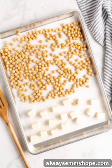 This vegan Buddha bowl is a flavor-packed meal brimming with caramelised roasted veggies, crispy chickpeas, tender baked tofu, and more! Overhead view of seasoned chickpeas and cubed tofu arranged on a parchment lined sheet pan.