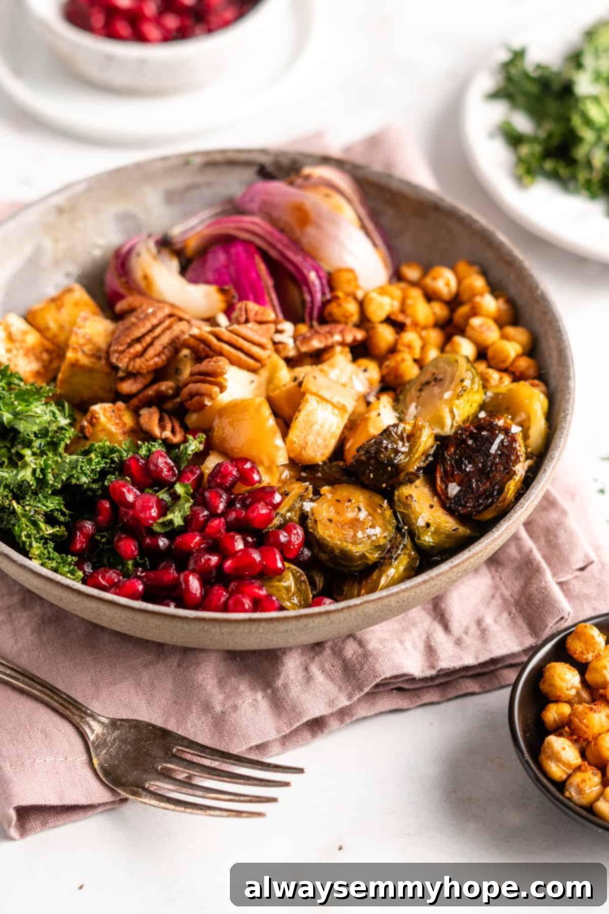 This vegan Buddha bowl is a flavor-packed meal brimming with caramelised roasted veggies, crispy chickpeas, tender baked tofu, and more! A beautifully assembled Buddha bowl filled with colorful ingredients including pomegranate seeds, kale chips, Brussels sprouts, chickpeas, tofu, apples, and onions.