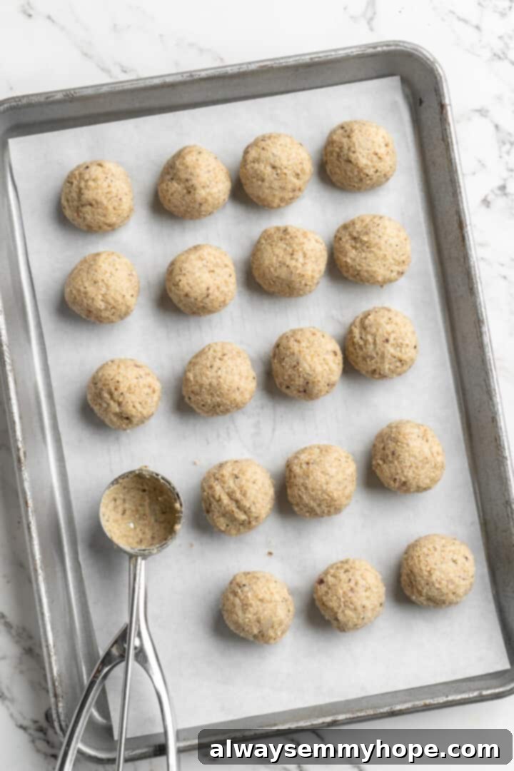 Overhead view of cookie dough scoop set on sheet pan of rolled meatballs