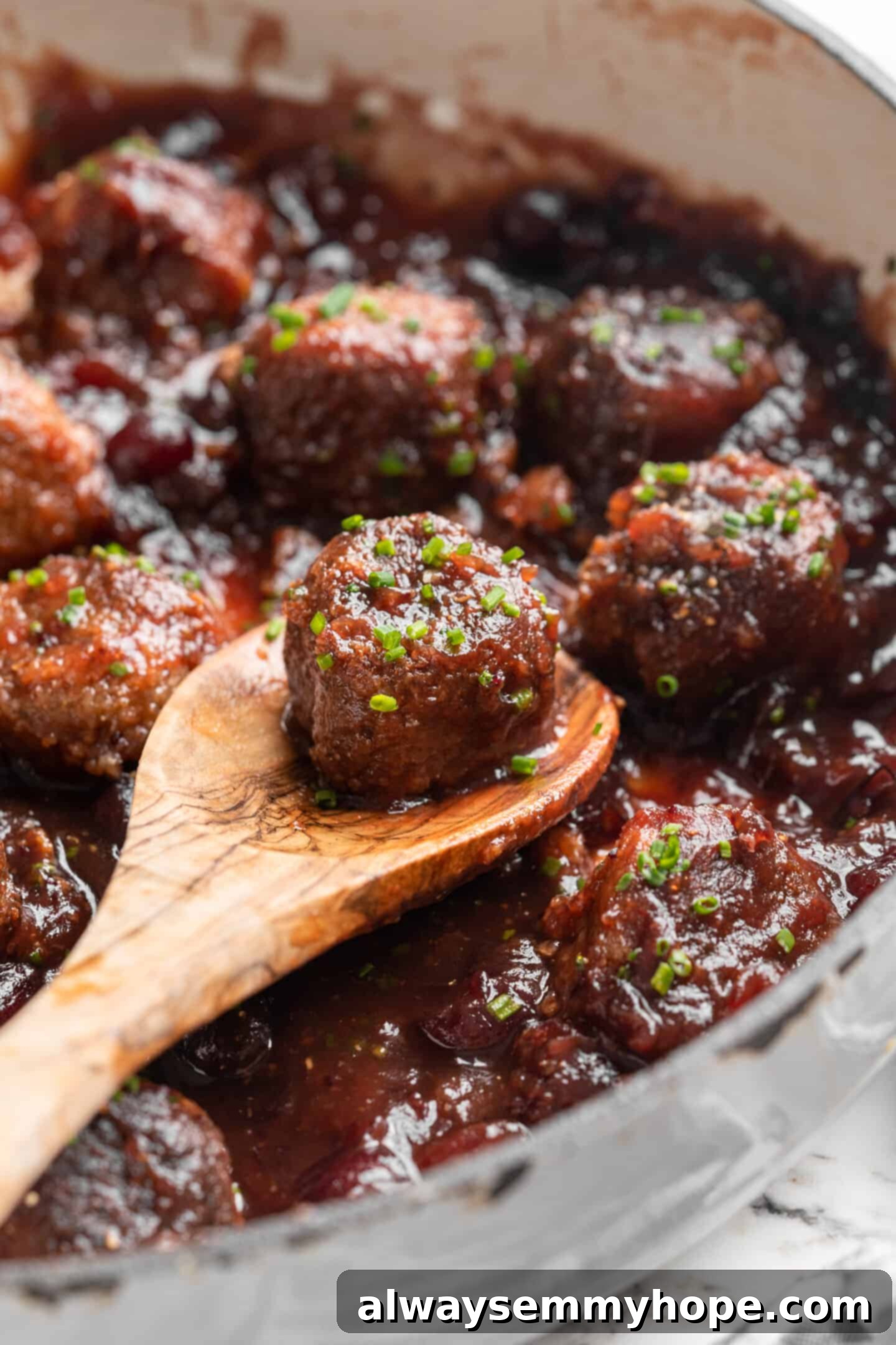 Skillet of vegan cranberry meatballs with wooden spoon lifting meatball from pan