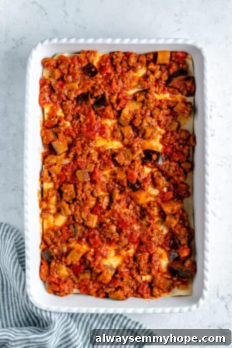 A layer of sauce, vegan meat, and eggplant on top of noodles.