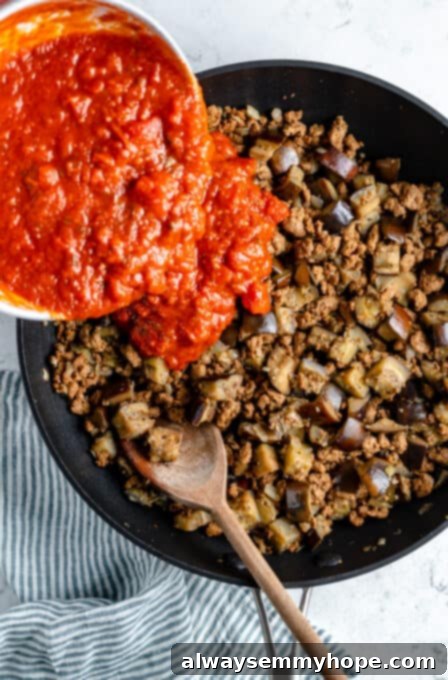 Tomato sauce poured into a pan of vegan meat and eggplant.