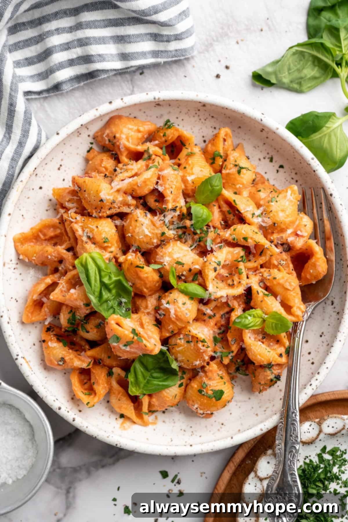 Overhead view of creamy tomato pasta in bowl with fork, garnished with fresh basil