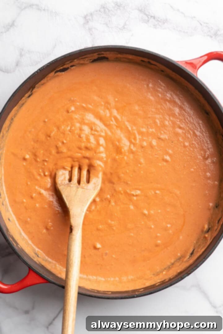 Close-up view of the vibrant vegan creamy tomato sauce being stirred in a skillet, showcasing its rich texture before adding pasta.