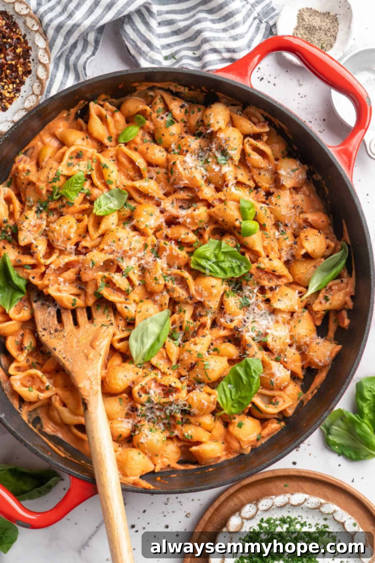 Overhead view of creamy tomato pasta simmering in a skillet, garnished generously with fresh basil leaves and a sprinkle of vegan Parmesan.