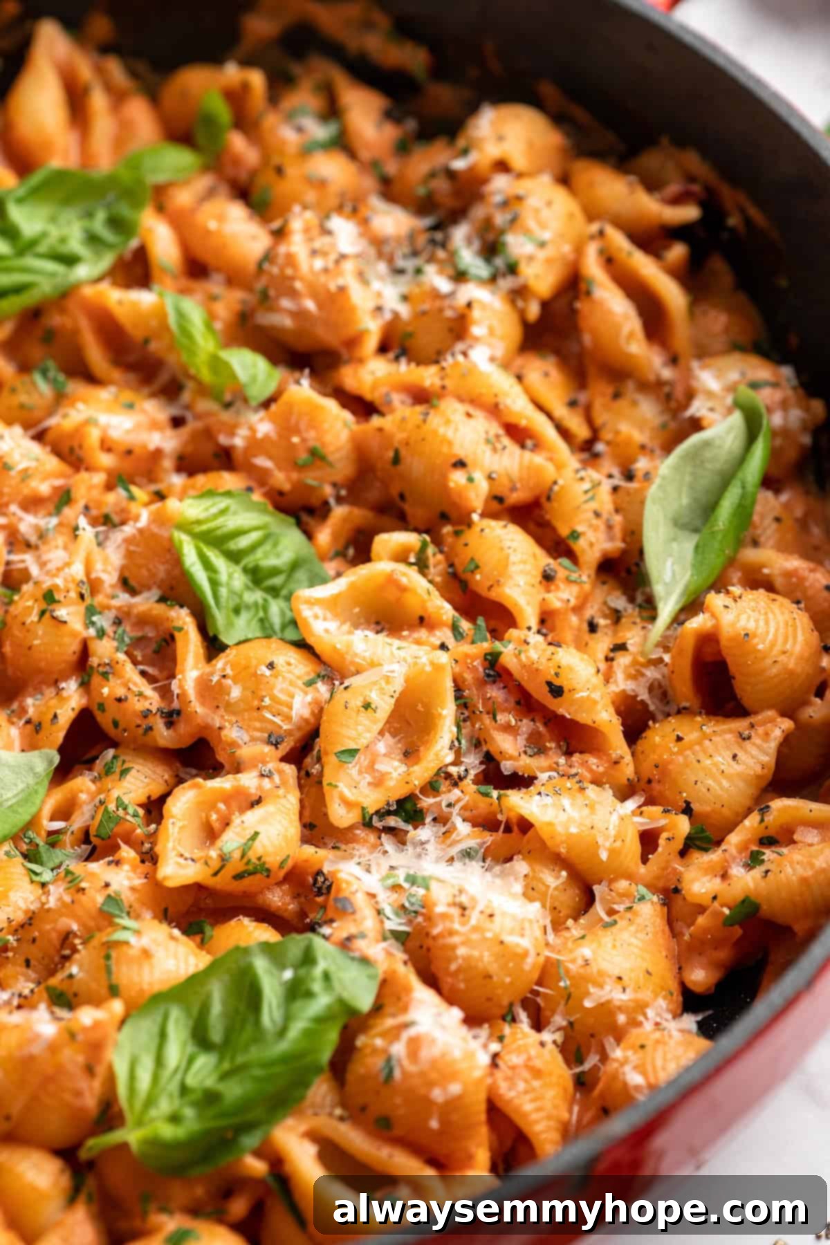 Close-up shot of creamy tomato pasta in a skillet, adorned with vibrant fresh basil leaves, ready to be served.