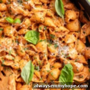 Overhead view of creamy tomato pasta in skillet with fresh basil leaves