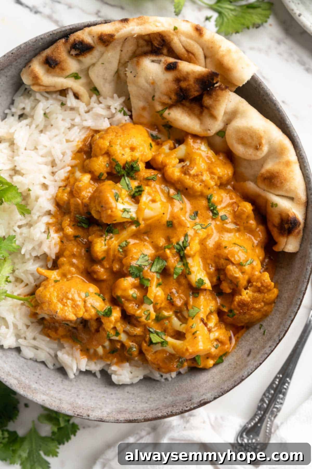 This vegan butter cauliflower starts by marinating the cauliflower in coconut and spices, making it extra delicious. Better than takeout! Overhead view of vegan butter cauliflower in bowl with rice and naan