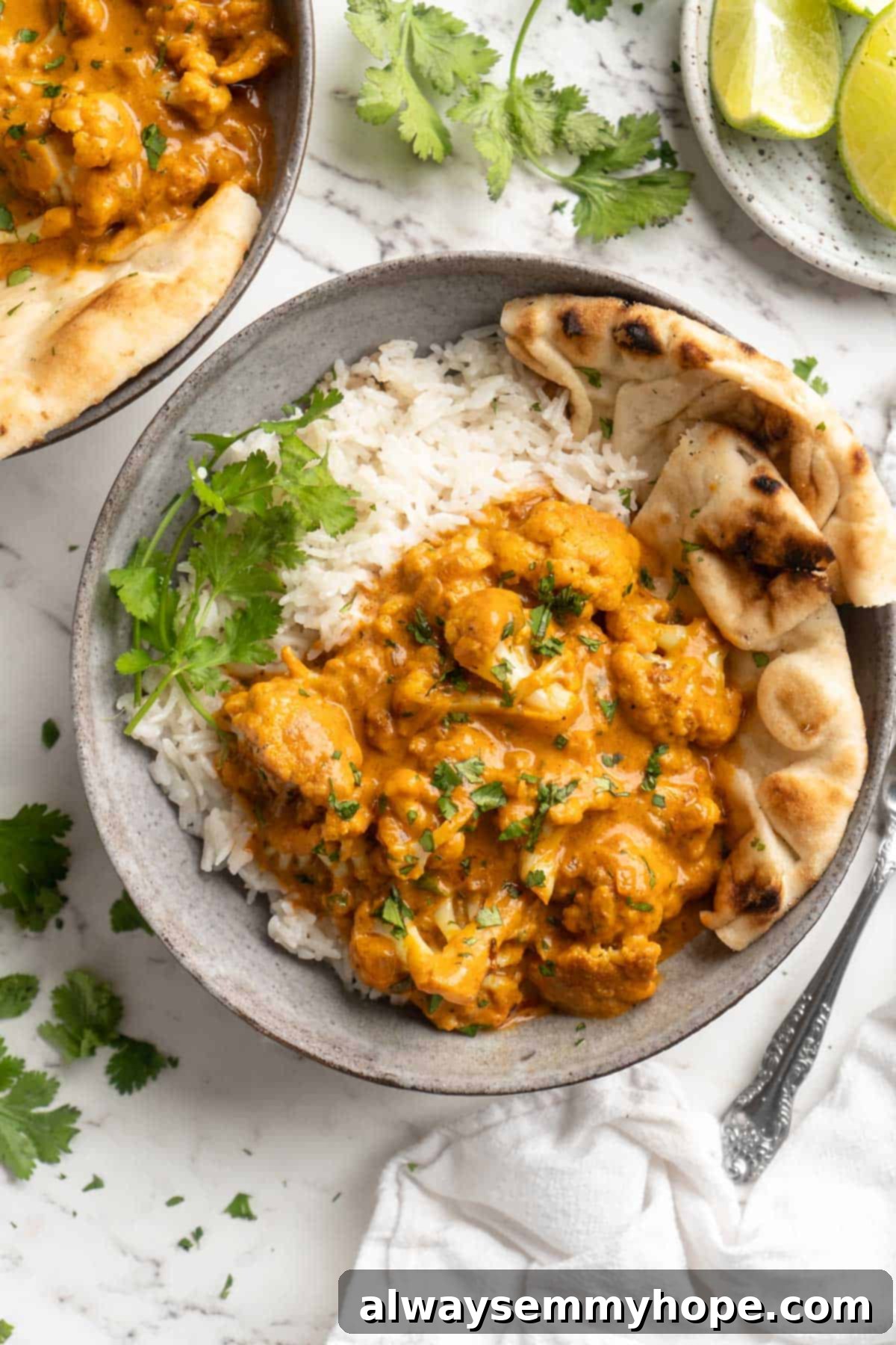 This vegan butter cauliflower starts by marinating the cauliflower in coconut and spices, making it extra delicious. Better than takeout! Overhead view of butter cauliflower in bowl with rice and naan