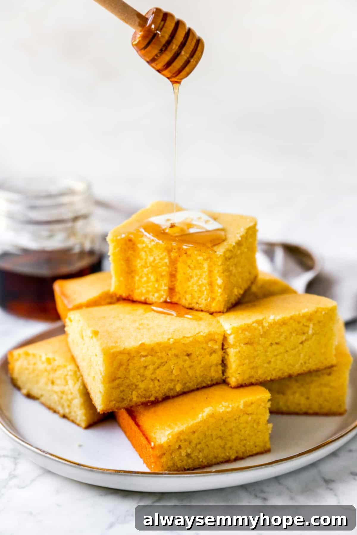 Stack of golden vegan cornbread muffins with a drizzle of maple syrup and a pat of vegan butter on top.