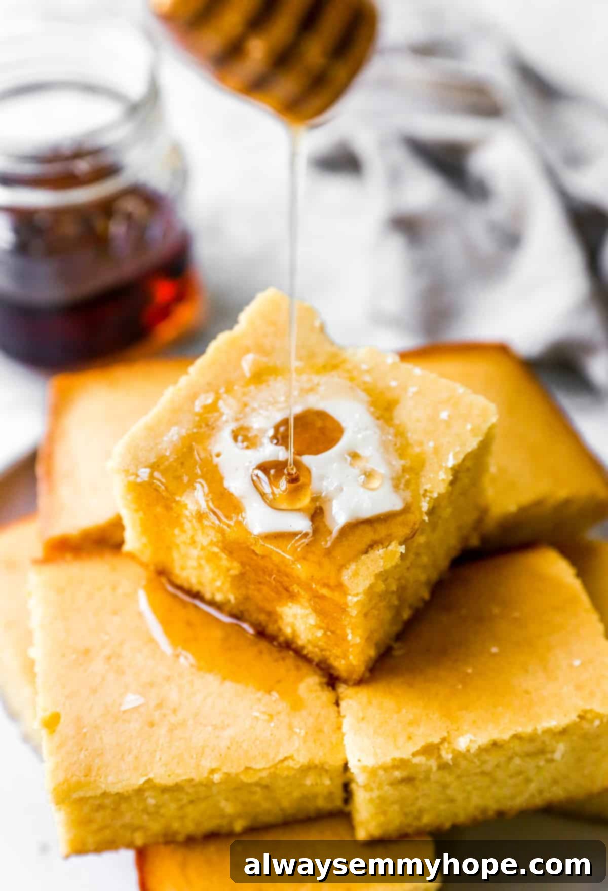 Close-up of a stack of fluffy vegan cornbread muffins, with a light drizzle of maple syrup and a melting pat of vegan butter.