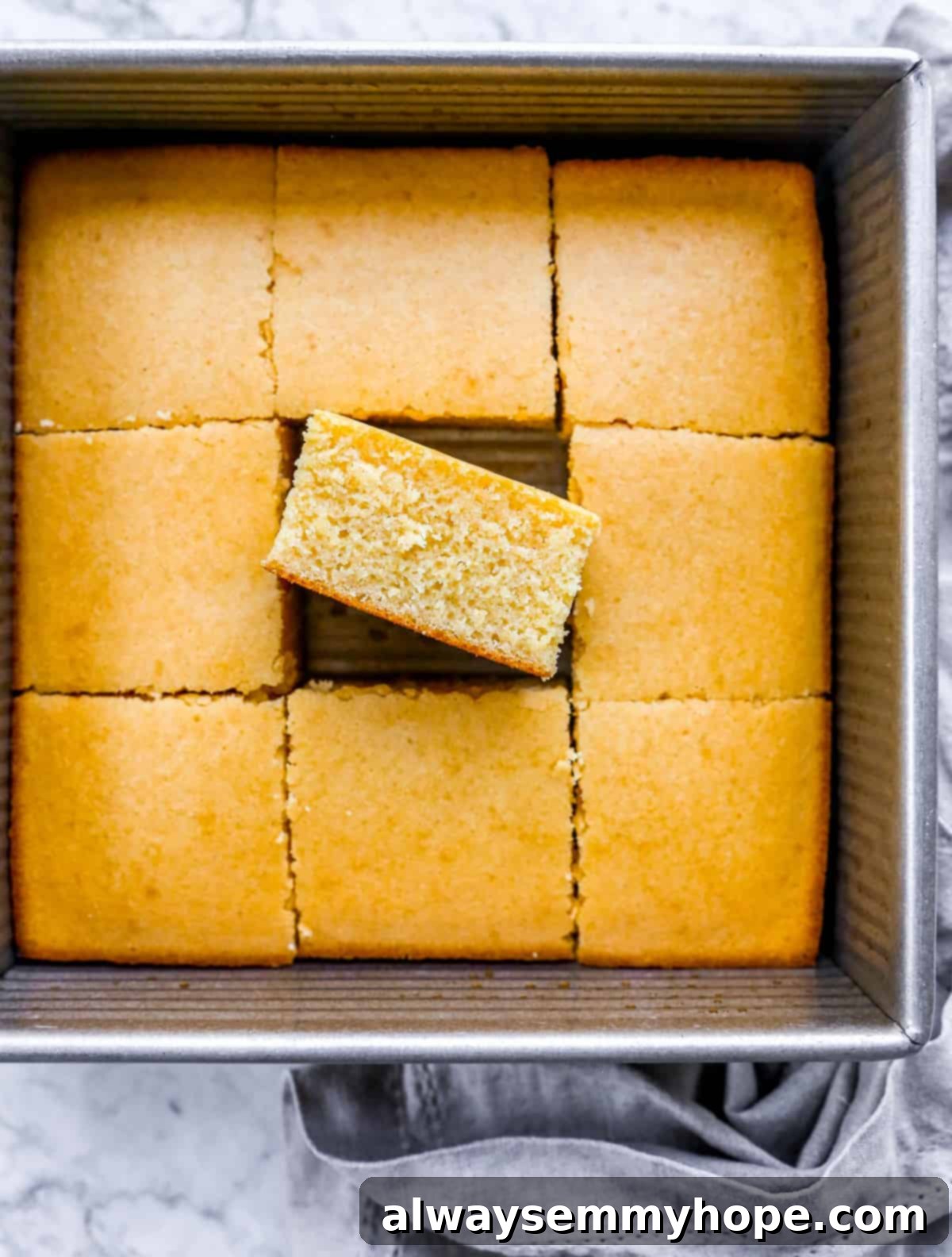 A pan of freshly baked cornbread, sliced with one piece slightly pulled out to show its fluffy interior.