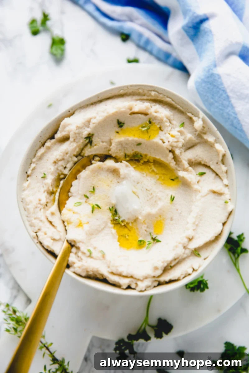 Top down view of mashed cauliflower in a bowl with a spoon, garnished with fresh thyme.