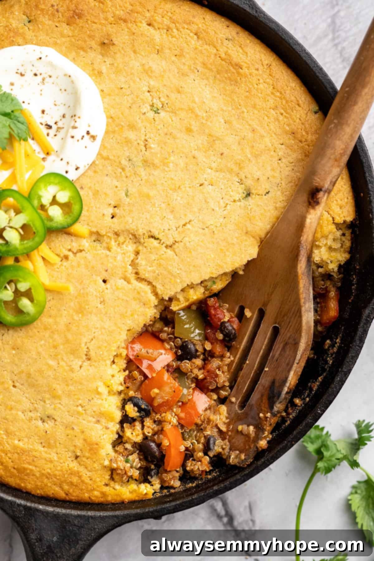 This vegan chili cornbread casserole is one of the BEST casseroles ever! The secret? Sweet, crispy cornbread baked on top of delicious chili. Wooden spoon digging into chili cornbread casserole, showcasing the layers of chili and cornbread
