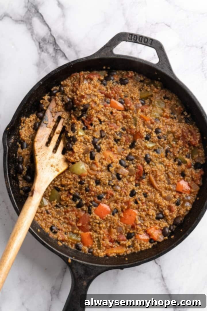This vegan chili cornbread casserole is one of the BEST casseroles ever! The secret? Sweet, crispy cornbread baked on top of delicious chili. Finished chili simmering in a skillet with a wooden spoon, ready for the cornbread topping