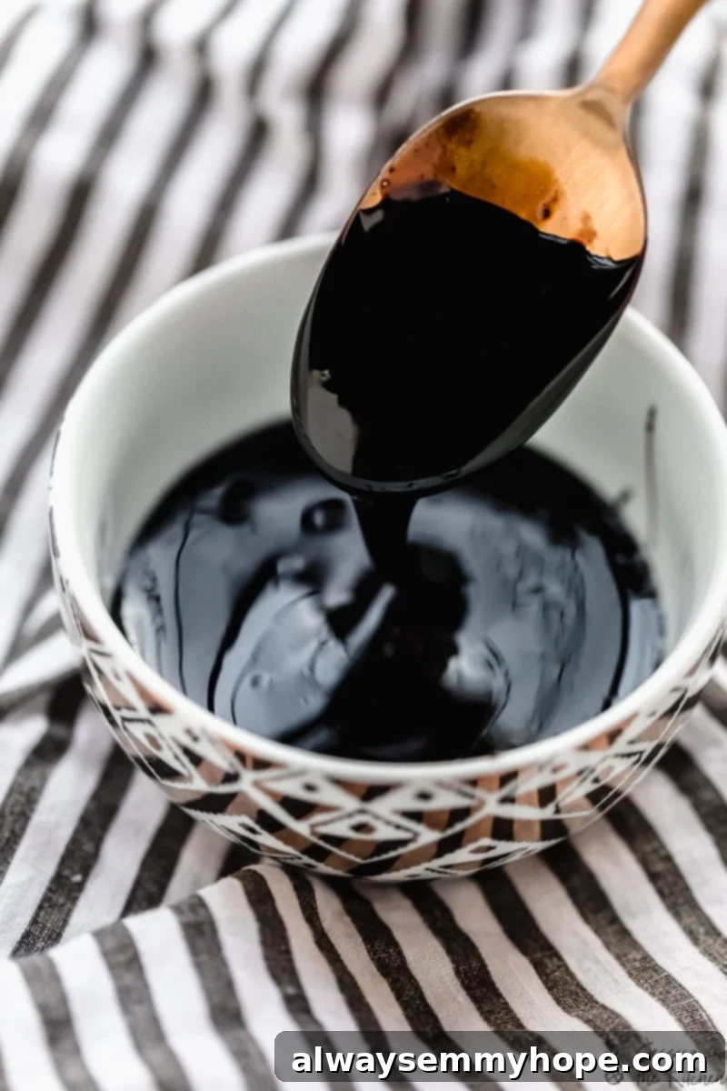 A spoon expertly dripping luscious homemade balsamic glaze into a small white bowl, showcasing its perfect syrupy consistency.