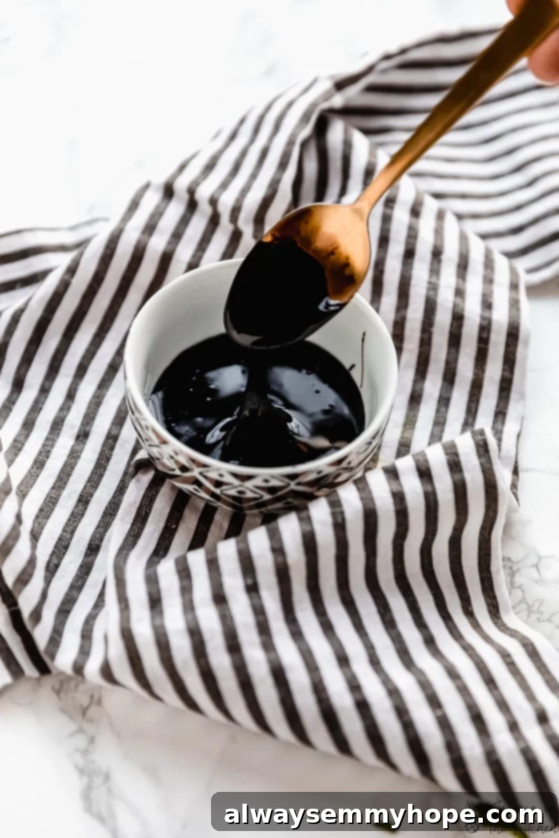 Here's how to make balsamic glaze in just 15 minutes! It's a delicious, sweet and tangy sauce perfect for drizzling on just about anything! Small bowl of balsamic glaze on striped cloth napkin with spoon dripping glaze into bowl