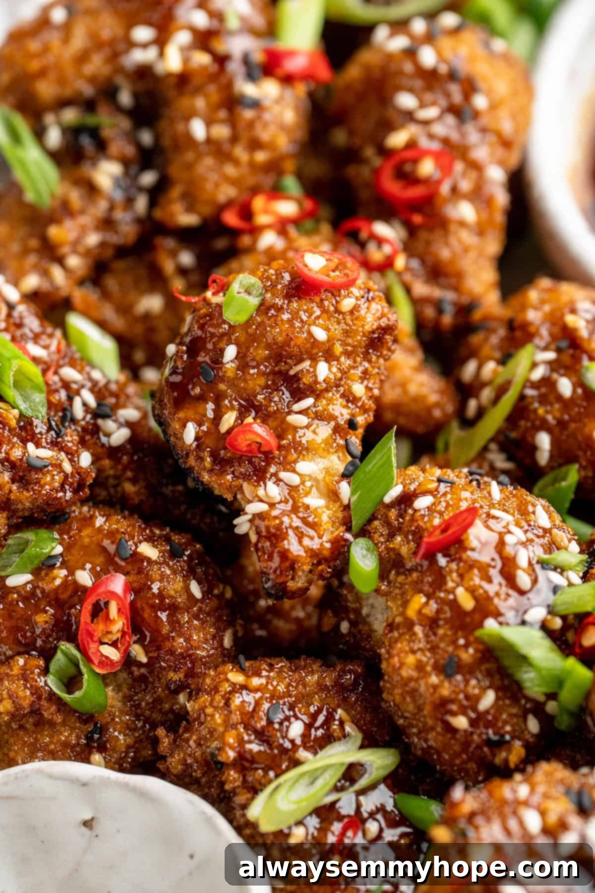 Extreme close-up of a crispy General Tso cauliflower floret, glistening with sauce and garnished with sesame seeds.