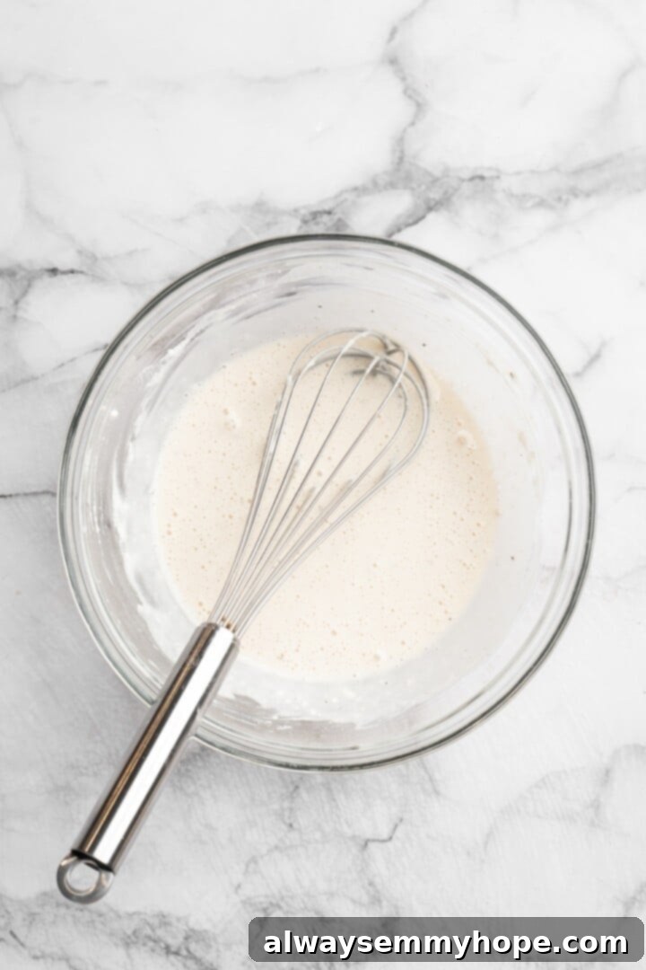 Overhead shot of a bowl with creamy, whisked batter for General Tso cauliflower, next to a whisk.