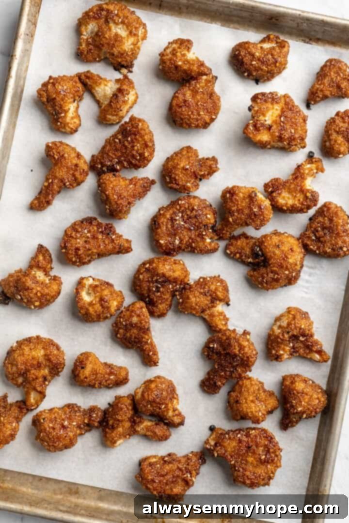 Sauce-coated General Tso cauliflower florets baked on a sheet pan, garnished with fresh scallions.
