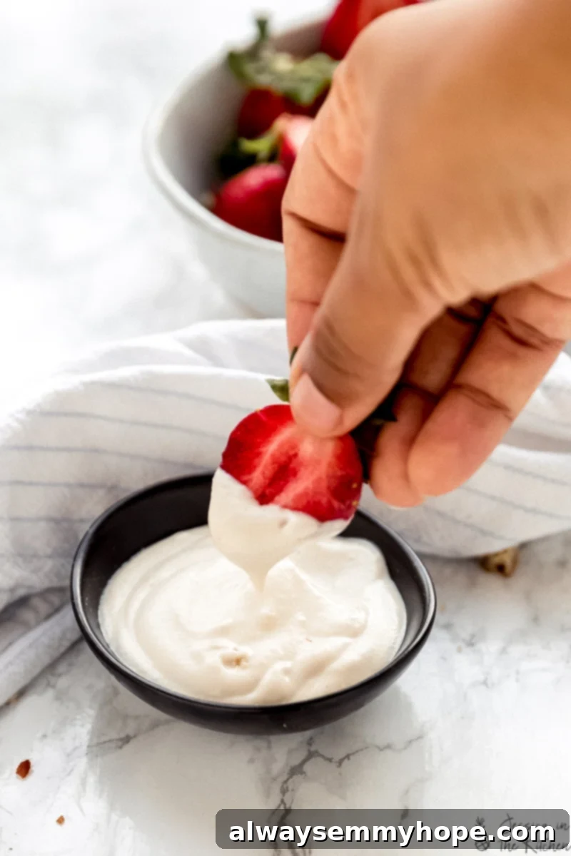 Vegan Cashew Whipped Cream 2 A hand dipping a fresh strawberry into a fluffy bowl of homemade vegan cashew whipped cream.