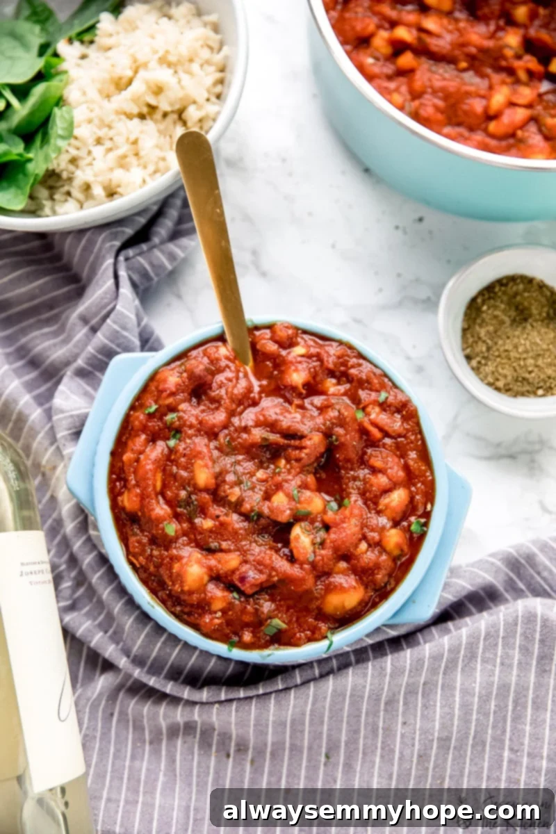 Velvety Smoked White Beans in Tomato Garlic Sauce 2 Top down view of creamy smoky white beans in garlicky tomato sauce in a blue pot. A spoon rests in the pot, highlighting the rich texture.