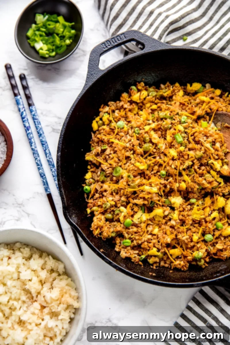 Top-down view of vibrant vegan cauliflower fried rice served in a sleek black skillet with elegant chopsticks resting alongside.
