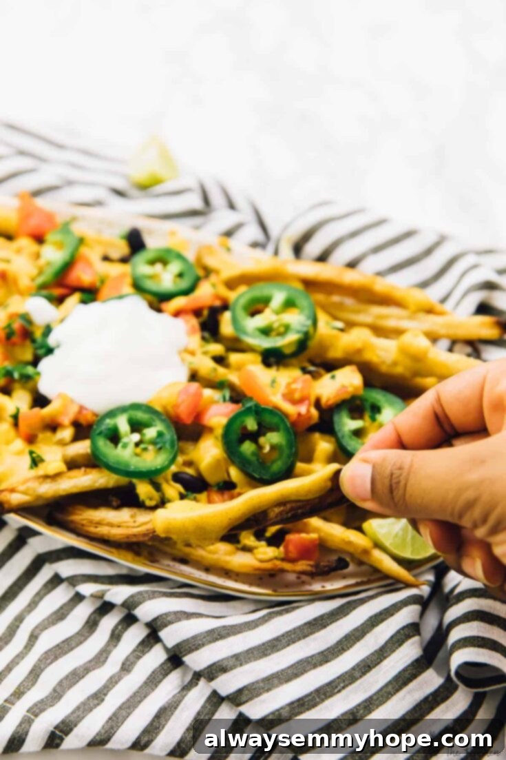 Score Big with 30 Vegan Super Bowl Recipes 22 Piled high Vegan Loaded Nacho Cheese Fries, topped with various ingredients.