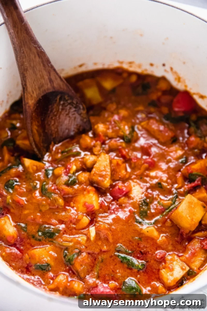 One-Pot Wonder Sweet Potato Curry 4 Sweet potato curry being stirred in a pot with a wooden spoon, showcasing its rich texture.