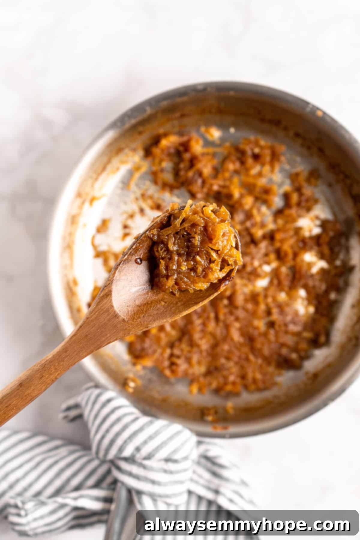 Learn how to caramelize onions the right way for sweet, deeply browned, jammy onions to add to your favorite meals and recipes! A wooden spoon lifting a scoop of perfectly caramelized onions above the skillet