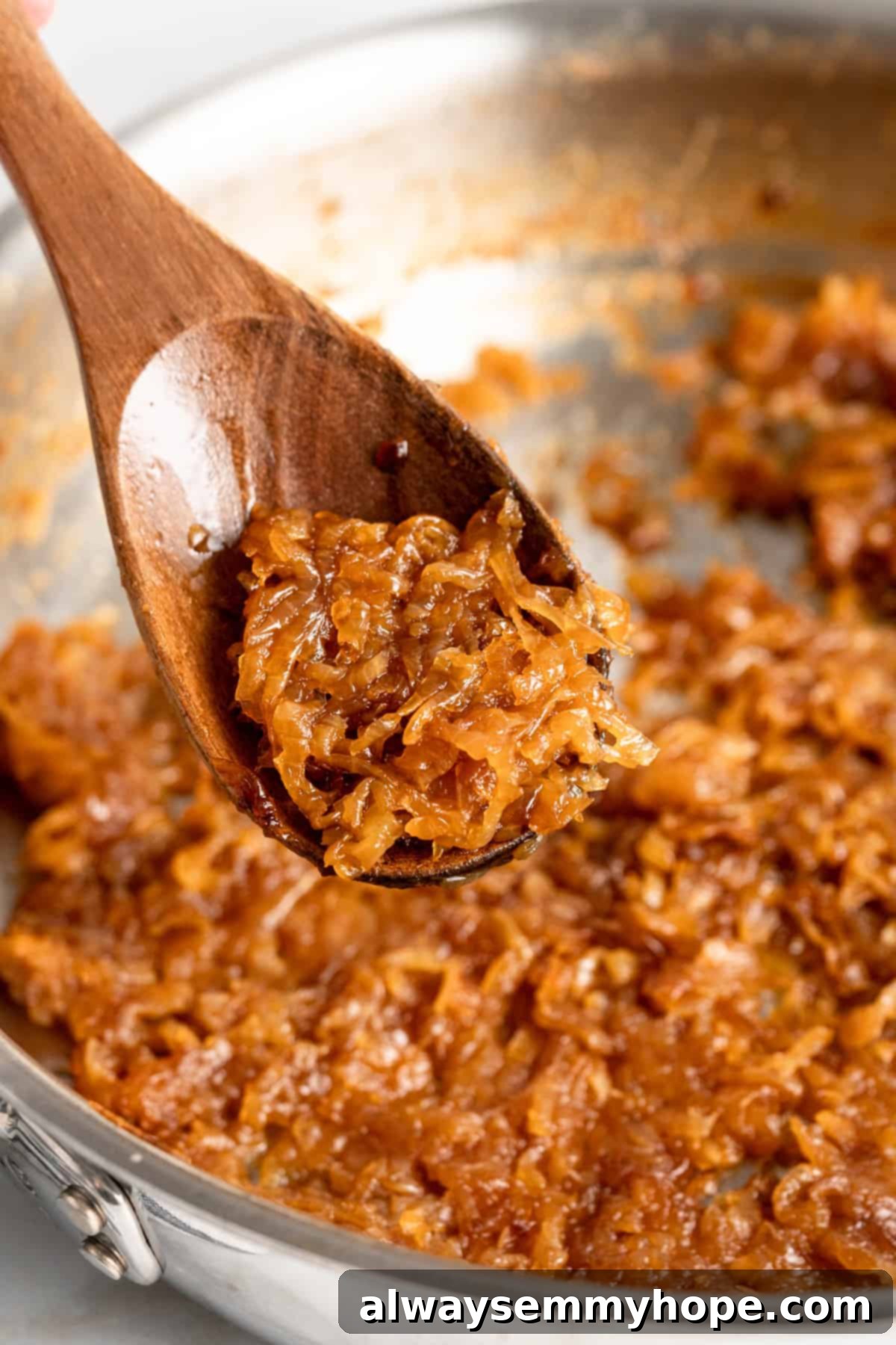 Learn how to caramelize onions the right way for sweet, deeply browned, jammy onions to add to your favorite meals and recipes! Closeup of caramelized onions on a wooden spoon with a pan out of focus in the background
