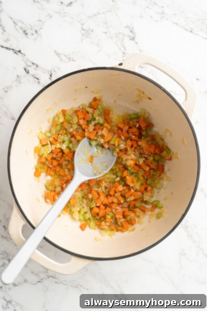 Overhead view of softened diced onions, carrots, and celery (mirepoix) sautéing in olive oil in a large pot.