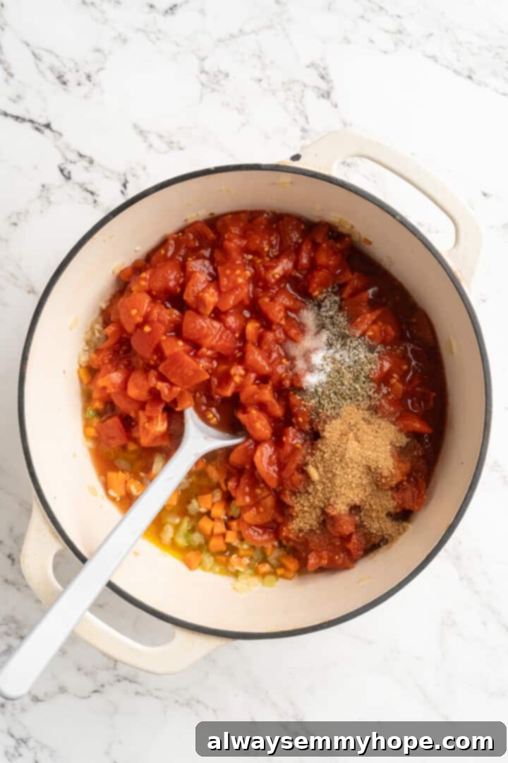 Overhead view of chopped tomatoes, sugar, oregano, salt, and pepper added to the softened mirepoix in the pot.
