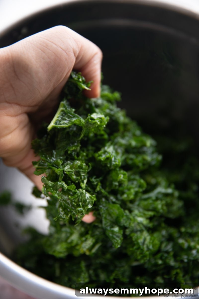 This is the BEST kale salad recipe! With tender massaged kale, avocado, carrots, and a crunchy seed blend tossed in creamy tahini dressing. A hand massaging kale leaves in a metal bowl.