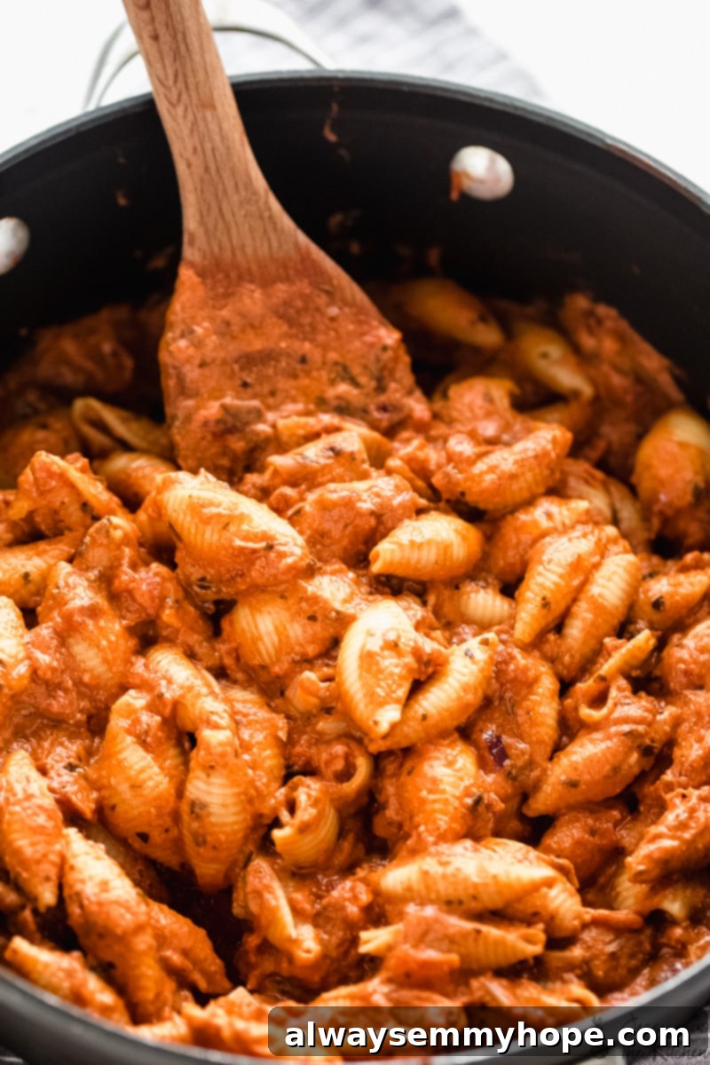 5 Steps to Affordable Vegan Eating 3 Pot of cooked creamy tomato pasta being stirred by a wooden spoon.