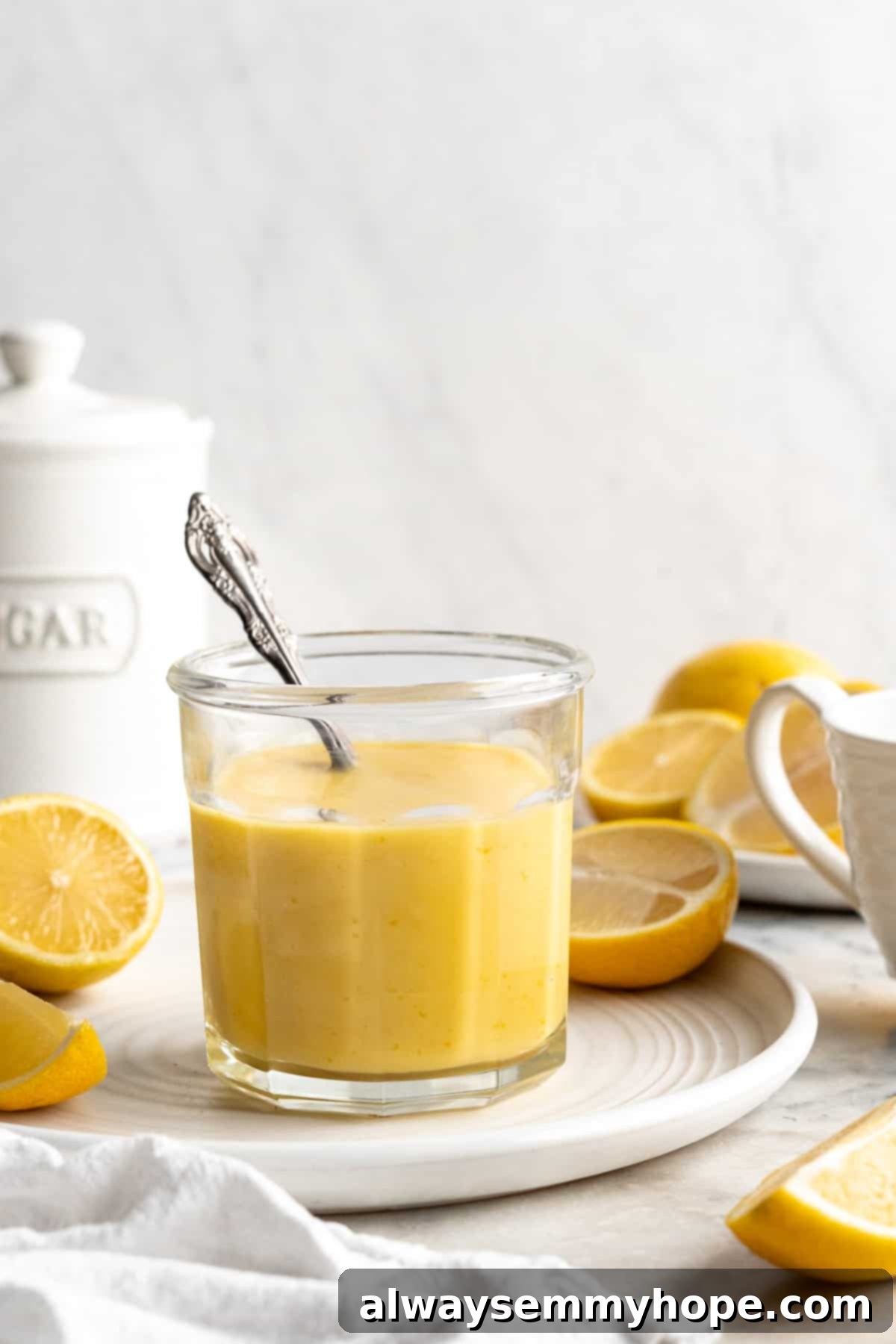 Jar of vegan lemon curd with spoon on plate with halved lemons