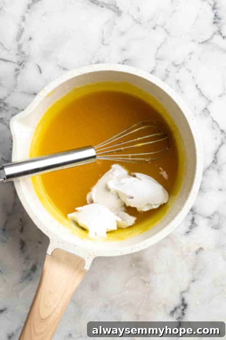 Overhead view of coconut cream added to saucepan of vegan lemon curd with whisk