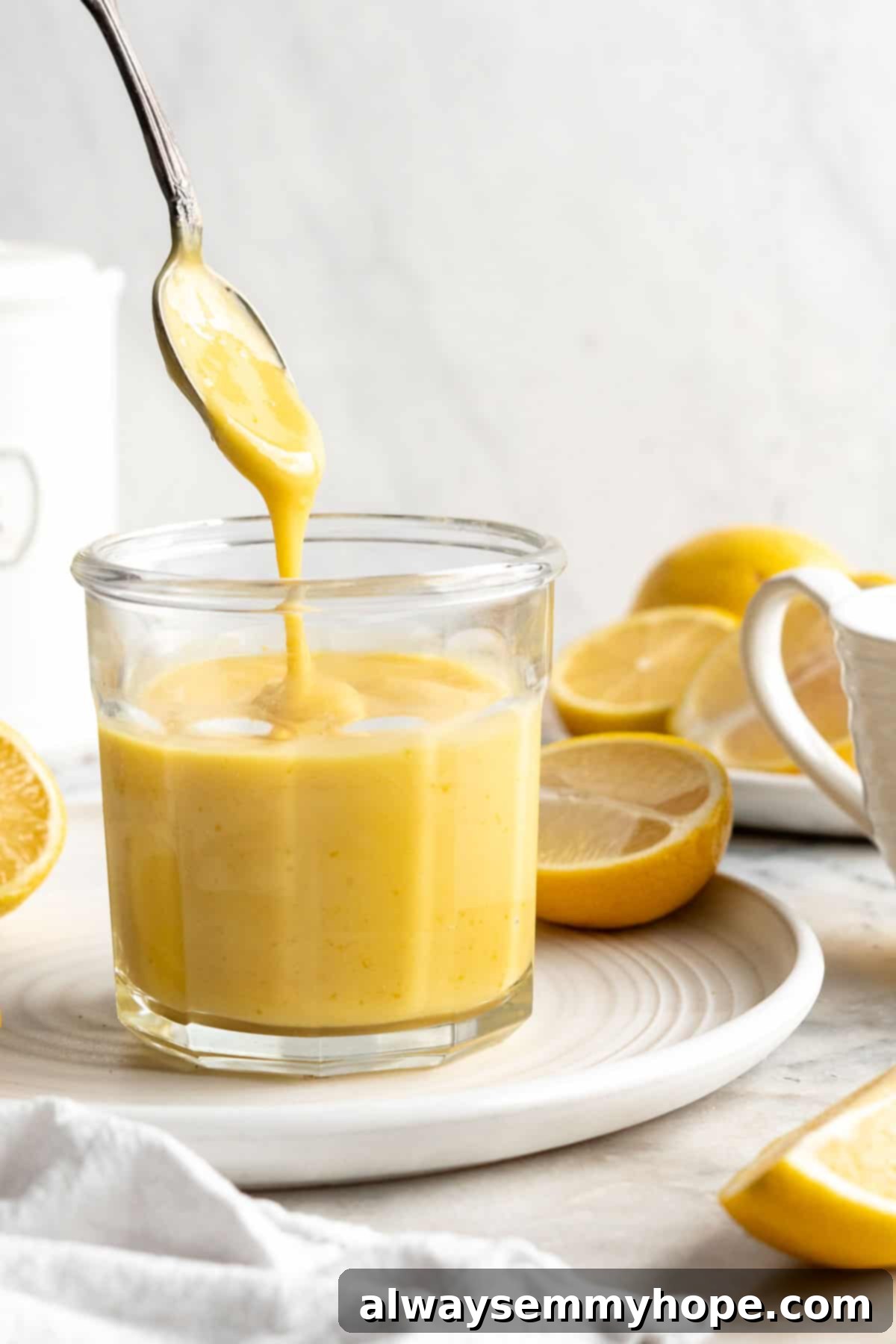 Spoon drizzling vegan lemon curd back into jar set on plate